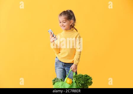 Petite fille avec de la nourriture dans le sac et téléphone mobile sur fond de couleur Banque D'Images