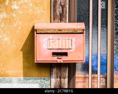 Vue avant d'une ancienne boîte aux lettres rouge attachée à un mur jaune à côté d'une fenêtre Banque D'Images