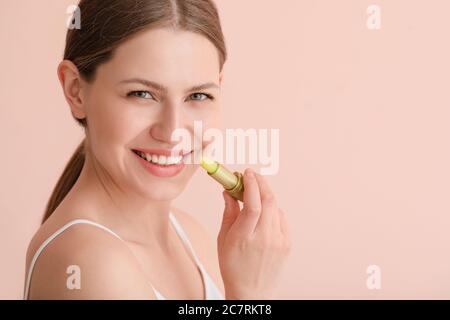 Belle jeune femme avec baume de lèvre sur fond de couleur Banque D'Images