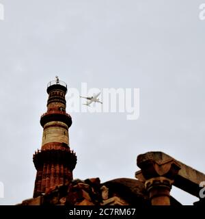 Avion volant dans le ciel nuageux pendant la journée près de Qutub Minar à Delhi Inde, avion volant haut dans le ciel Banque D'Images