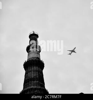 Avion volant dans le ciel nuageux pendant la journée près de Qutub Minar à Delhi Inde, avion volant haut dans le ciel Banque D'Images