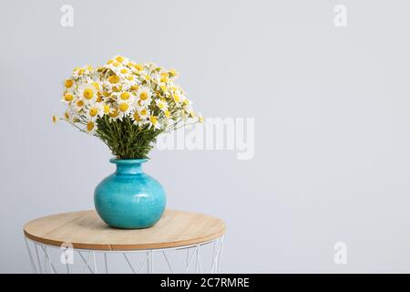 Vase avec de belles chamomiles sur la table contre fond clair Banque D'Images