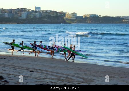 Un groupe de surfeurs descendent la plage jusqu'à l'eau à Manley, Sydney, Nouvelle-Galles du Sud, Australie. Banque D'Images