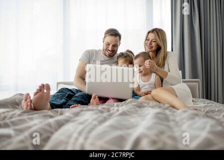Adorable couple allongé sur le lit et regardant quelque chose sur l'ordinateur portable avec leurs enfants Banque D'Images