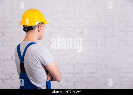 vue arrière de l'homme en uniforme bleu de constructeur regardant le mur de brique blanche Banque D'Images