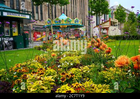 Vue à travers les fleurs d'été colorées : Corneliusplatz dans le centre-ville de Düsseldorf avec un kiosque à journaux et un carrousel nostalgique. Banque D'Images