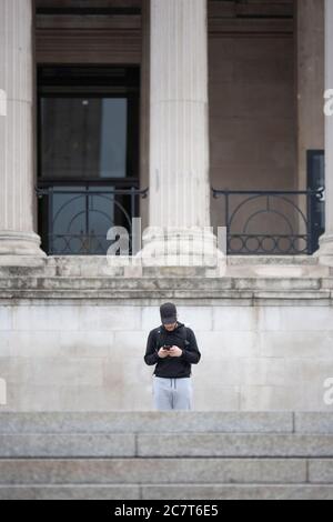 Un homme se tient devant la galerie nationale en regardant son smartphone. Trafalgar Square, Londres, Angleterre, Royaume-Uni Banque D'Images