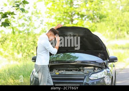Jeune homme près d'une voiture brisée sur la route Banque D'Images