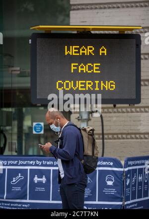 Homme, portant un masque et regardant son téléphone mobile, se tient devant un panneau qui indique "PORTER UN MASQUE". Londres, Royaume-Uni Banque D'Images