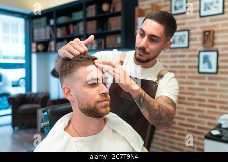 Coiffeur jeune avec tatouages coiffant les cheveux de la cliente un barbershop Banque D'Images