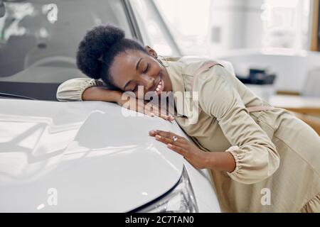 belle femme afro rêve de nouvelle voiture, jeune femme est venue voir des automobiles, faire l'achat. femme est penchée sur la voiture blanche luxueuse, souriant Banque D'Images