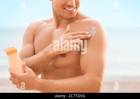 Jeune homme appliquant de la crème solaire sur la plage Banque D'Images