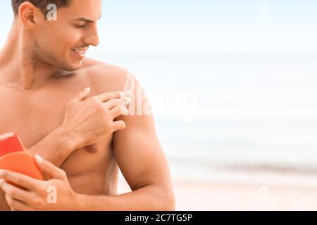 Jeune homme appliquant de la crème solaire sur la plage Banque D'Images