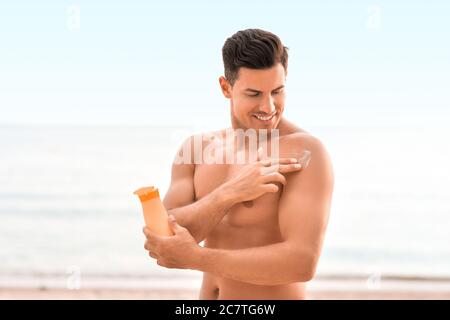 Jeune homme appliquant de la crème solaire sur la plage Banque D'Images