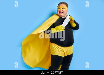 portrait de drôle caucasien gros homme avec rouleau de papier toilette dans les mains, l'homme porte le costume noir et jaune avec masque, il regarde côté avec peur f Banque D'Images