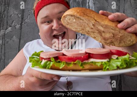 comic caucasien embonpoint homme ouvre à l'intérieur de sandwich, regarde les ingrédients. nutrition, malsain concept de style de vie Banque D'Images