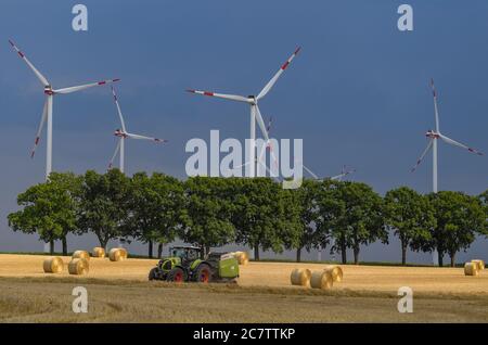 Petersdorf, Allemagne. 19 juillet 2020. Des nuages de tempête sombres se déplacent sur un parc éolien tandis qu'en premier plan un agriculteur presse la paille en rouleaux. Credit: Patrick Pleul/dpa-Zentralbild/dpa/Alay Live News Banque D'Images