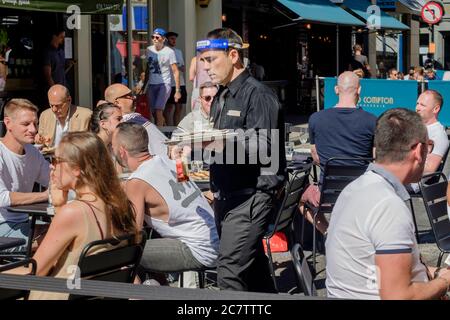 18 juillet 2020. Les rues de la zone de Soho, dans le centre de Londres, ont été piétonnes pour permettre aux bars et restaurants de mettre en place des places assises en plein air afin de maintenir les distances sociales entre les clients, les mesures d'assouplissement Covid-19 étant mises en œuvre par le gouvernement : Un serveur portant un masque de protection est disponible dans un espace extérieur situé dans Old Compton Street, Soho, Londres, Royaume-Uni. Banque D'Images