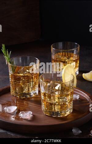 Trois verres de whisky froid au romarin, zestes de citron sur fond brun foncé. Orientation verticale. Banque D'Images