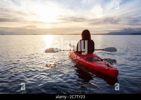 Kayak de mer dans des eaux calmes pendant un coucher de soleil coloré et vibrant. Banque D'Images