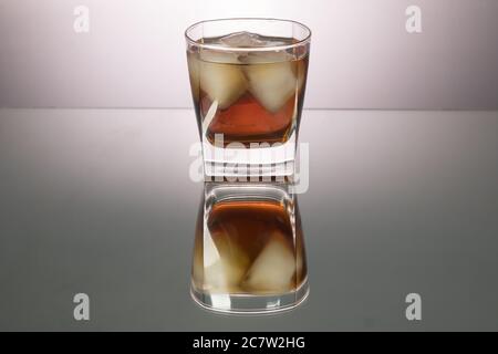 Verre de whisky avec morceaux de glace sur la table miroir. Image horizontale avec espace de copie. Banque D'Images