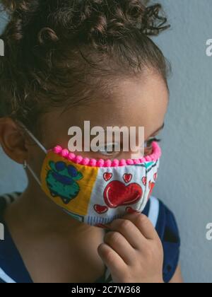 Une petite fille avec un masque avec des coeurs regarde sur le côté avec sa main sur son menton Banque D'Images