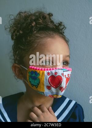 Une petite fille avec un masque avec des coeurs regarde sur le côté Banque D'Images