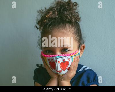 Une petite fille avec un masque avec les coeurs regarde l'appareil photo et embrassant son visage Banque D'Images