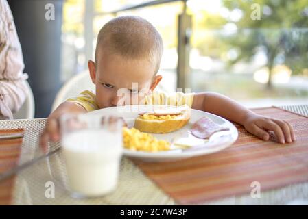 Petit foyer d'un enfant malheureux assis devant la table avec de la nourriture sur elle Banque D'Images