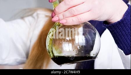 Gros plan, une fille verse du liquide vert dans le flacon en faisant de la formule verte dans le bol. Concept de science ou d'éducation. Banque D'Images