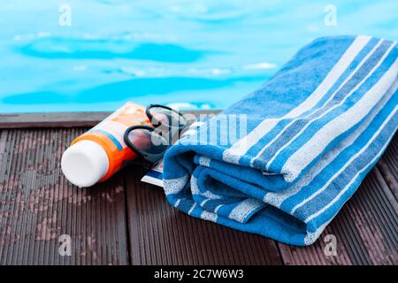 lunettes de soleil, tube de crème solaire, serviette bleue près de la piscine, fond tropical Banque D'Images