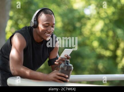 Joyeux homme sportif noir bavardant au téléphone, buvant des protéines Banque D'Images