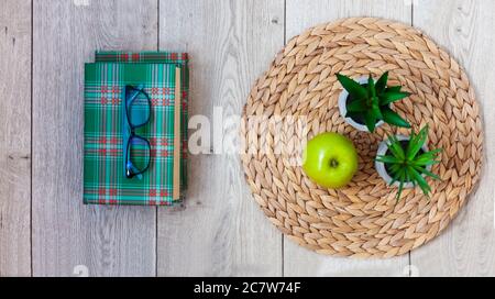 De retour à l'école, pile de livres en couvertures vertes, verres, pomme verte et plantes en pots sur un support en osier sur une table en bois. Enseignement à distance. C'est Banque D'Images