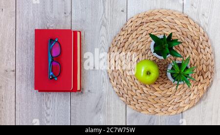 De retour à l'école, pile de livres en couvertures rouges, verres, pomme verte et plantes en pots sur un support en osier sur une table en bois. Enseignement à distance. Quara Banque D'Images