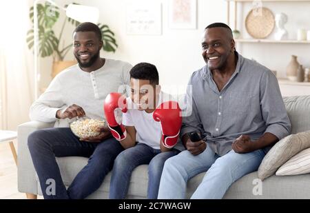 Papa noir, son et grand-père regardant le match de boxe à la télévision et applaudissent Banque D'Images