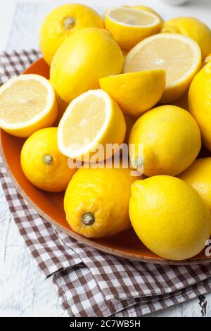 Citrons, certains coupés ouverts, dans un bol orange avec un chiffon à carreaux sur une table blanche. Banque D'Images