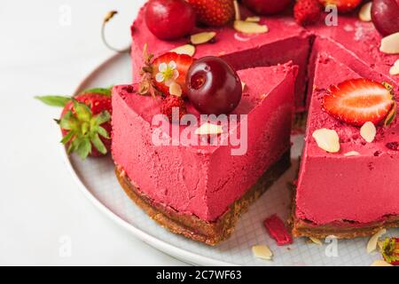 Tranche de gâteau au fromage vegan aux baies ou gâteau avec cerises fraîches et fraises dans un plat. Gros plan. Dessert végétalien sain Banque D'Images