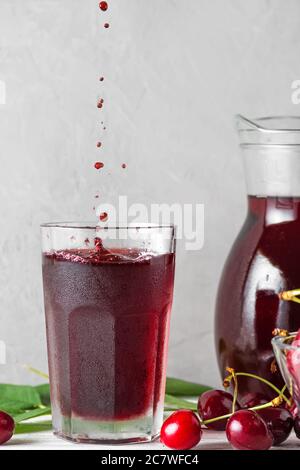 Jus de cerise dans un verre avec gouttes et jus de fruits et baies fraîches sur fond blanc. Rafraîchissement en été. Orientation verticale Banque D'Images