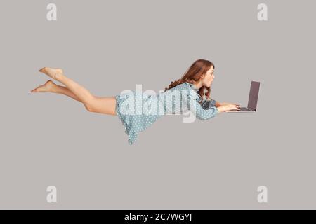 Vol stationnaire dans l'air. Surprise excitée fille ruffle robe lévitant avec ordinateur portable, dactylographiant le clavier, lisant choquant message d'actualité sur l'ordinateur tout en volant moi Banque D'Images