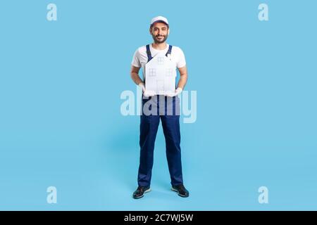 Homme de main pleine longueur, ouvrier de bâtiment en uniforme tenant maison de papier. Un gars de déménageur offrant de l'aide dans la réinstallation, les services de réparation à domicile et l'entretien. ind Banque D'Images