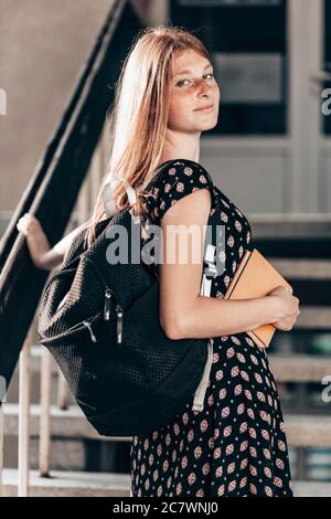 Jeune fille, gingembre, jeune fille d'école devant son école, avec un sac à dos, en train de regarder heureux Banque D'Images