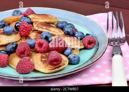 Petites crêpes aux baies et au sirop d'agave dans une assiette sur une table en bois Banque D'Images