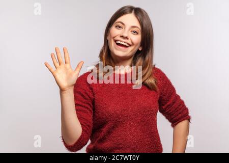 Bonjour, je suis ravi de vous rencontrer! Portrait de la bonne fille de brunette dans shaggy sweater levant la main en agitant salut et souriant amical, regardant la caméra avec hospita Banque D'Images