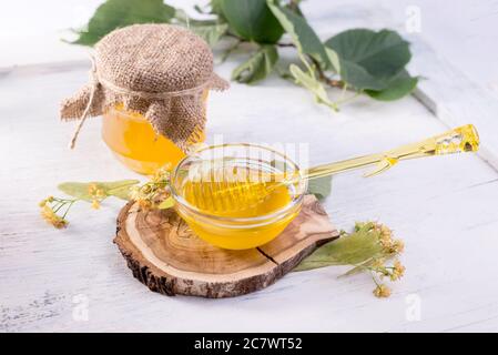 Linden miel en pot et bol avec un balancier au miel sur une table en bois blanc. Branche défocused de linden au premier plan. Banque D'Images