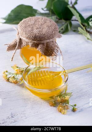 Linden miel en pot et bol avec un balancier au miel sur une table en bois blanc. Branche défocused de linden au premier plan. Banque D'Images