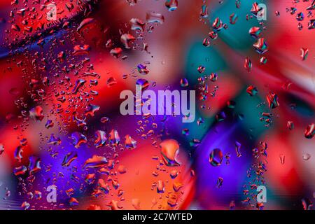 Arrière-plan abstrait pittoresque avec gouttes de pluie sur verre, lumières de ville au néon. Teintes claires de bleu, rouge et vert. Motif moderne tendance, papier peint ou Banque D'Images