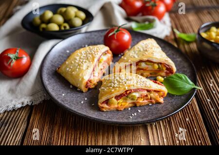 Délicieux feuilletés feuilleté pizza triangle rouleaux farcis avec sauce tomate, jambon, fromage, maïs, olives et arrosé de graines de sésame Banque D'Images