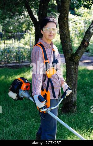 Portrait d'une jardinière féminine avec coupe-herbe dans l'arrière-cour. Concept de travail de jardin. Banque D'Images