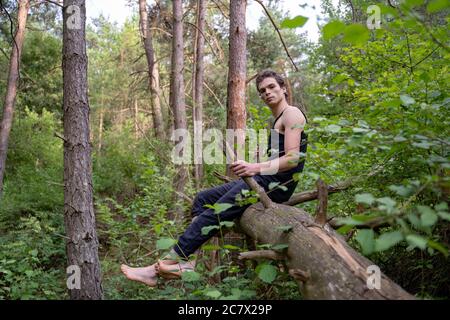 Vue latérale d'un homme attentionné assis en bois contre les arbres dans la forêt Banque D'Images