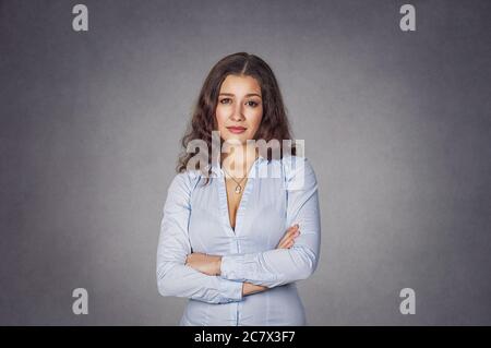 Portrait d'une femme mécontent sceptique et en colère debout avec des bras repliés sur fond gris studio. Mannequin fille, long ondulé cheveux bouclés en bleu formel Banque D'Images